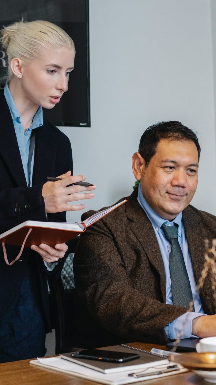 ethnic male lawyer showing document on laptop to young female colleague